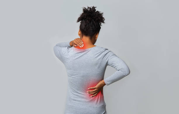 one lady are grey t-shirt showing a Back view of african woman rubbing her inflamed neck and loins.